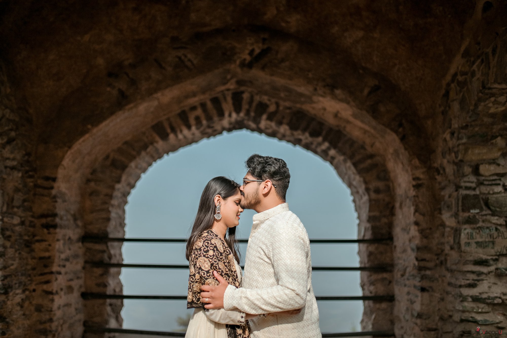 Ethnic couple enjoying a serene moment on a fort rooftop, with a sweet kiss on her forehead.